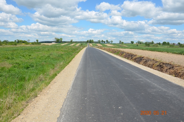 Asfaltowa droga na tle zielonych i żółtych pól pod niebieskim niebem z chmurami.