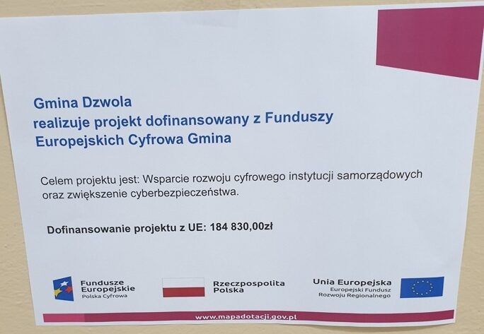 Tablica z napisem o projekcie dofinansowanym z Funduszy Europejskich Cyfrowa Gmina, z logotypami Funduszy Europejskich, Polski i Unii Europejskiej, biały i różowy kolor.