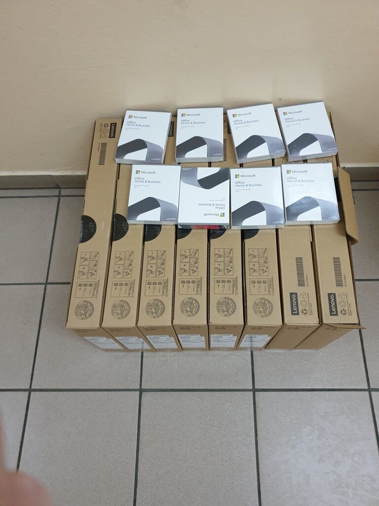 Siedem kartonowych pudełek Lenovo ustawionych pionowo na podłodze, na nich osiem białych opakowań Microsoft Office Home & Business.