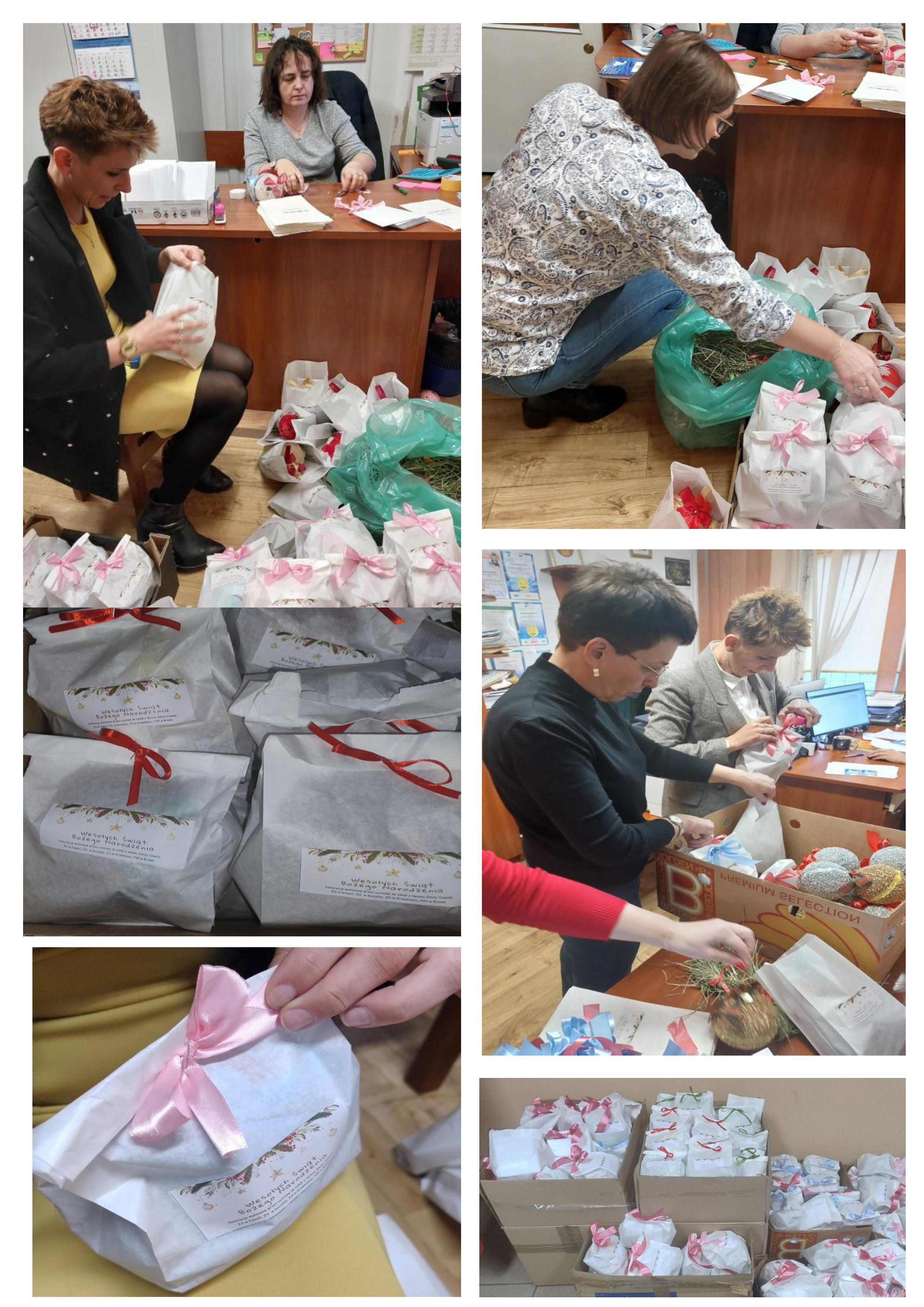 Kobiety pakujące białe papierowe torby z różowymi i czerwonymi wstążkami, pudełka z sianem, ozdoby świąteczne, kartki z życzeniami, drewniana podłoga i meble biurowe.