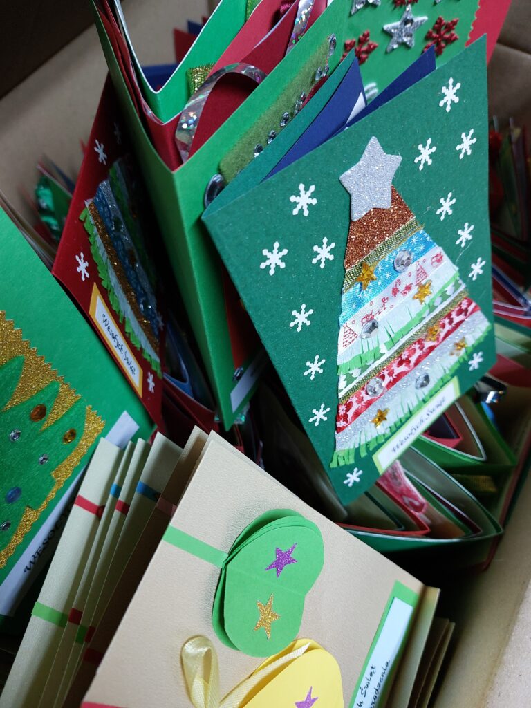 Ręcznie robione kartki świąteczne w pudełku, ozdobione wycinankami, gwiazdkami, cekinami i napisami "Wesołych Świąt". Kolory zielony, czerwony, beżowy, złoty i srebrny.