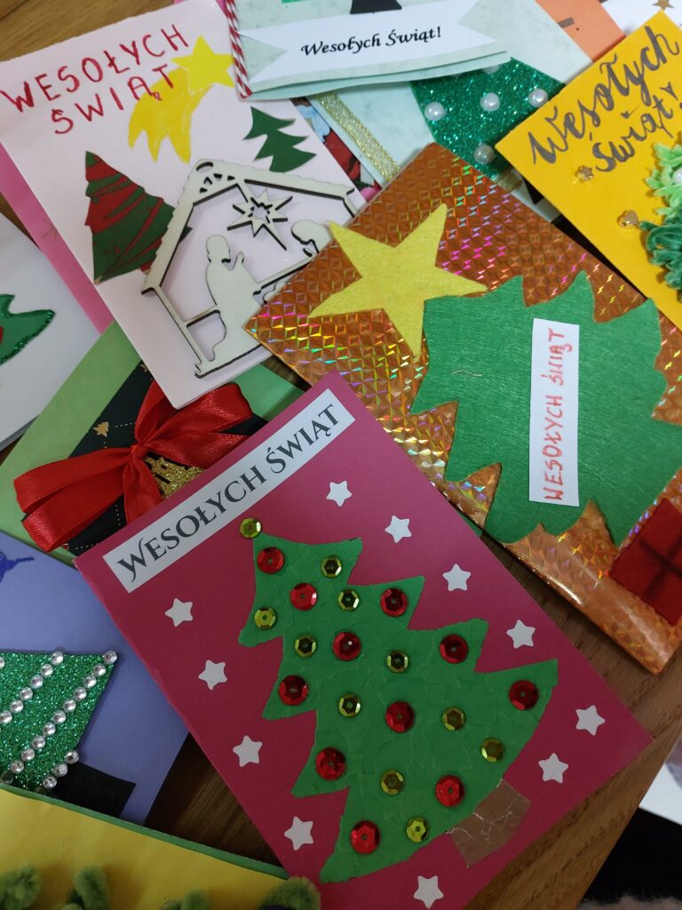 Kartki świąteczne z zielonymi choinkami, czerwonymi i złotymi cekinami, żółtymi gwiazdami, czerwoną kokardą i napisem "Wesołych Świąt" na różnokolorowych tłach.