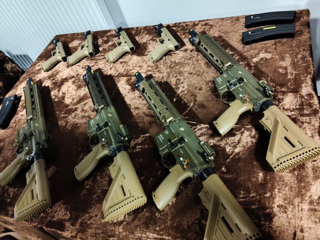 Trzy karabiny i cztery pistolety w kolorze piaskowym oraz zielonym, dwa magazynki, ułożone na brązowym materiale.