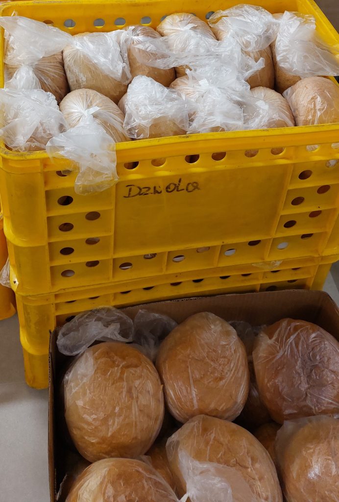 Żółte plastikowe skrzynki i karton wypełnione okrągłymi bochenkami chleba owiniętymi przezroczystą folią.