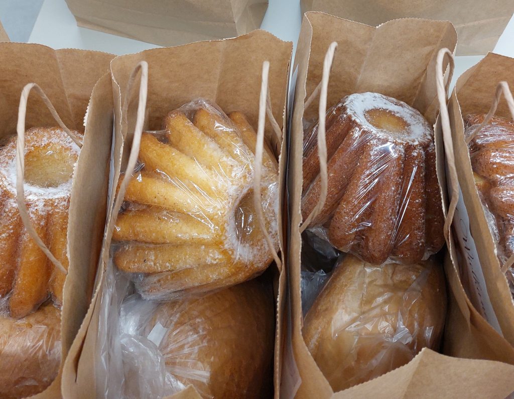 Brązowe papierowe torby z uchwytami, w środku opakowane w folię babki i bochenki chleba o złotobrązowym kolorze.