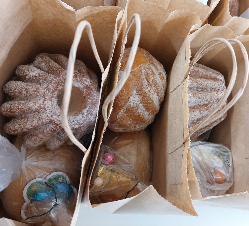 Brązowe papierowe torby z wypiekami pokrytymi cukrem pudrem oraz plastikowymi torebkami z kolorowymi jajkami czekoladowymi.