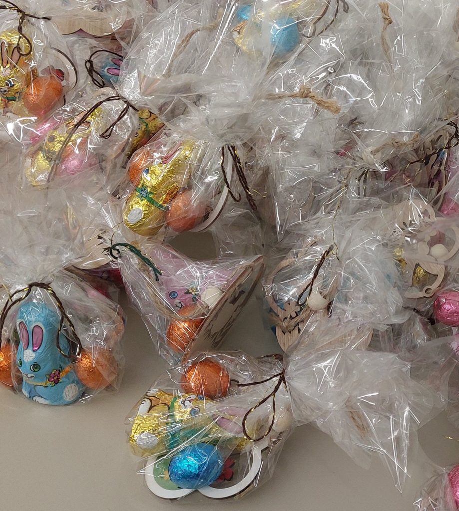 Przezroczyste woreczki z kolorowymi czekoladowymi zajączkami i jajkami w folii, przewiązane brązowymi i złotymi sznureczkami.