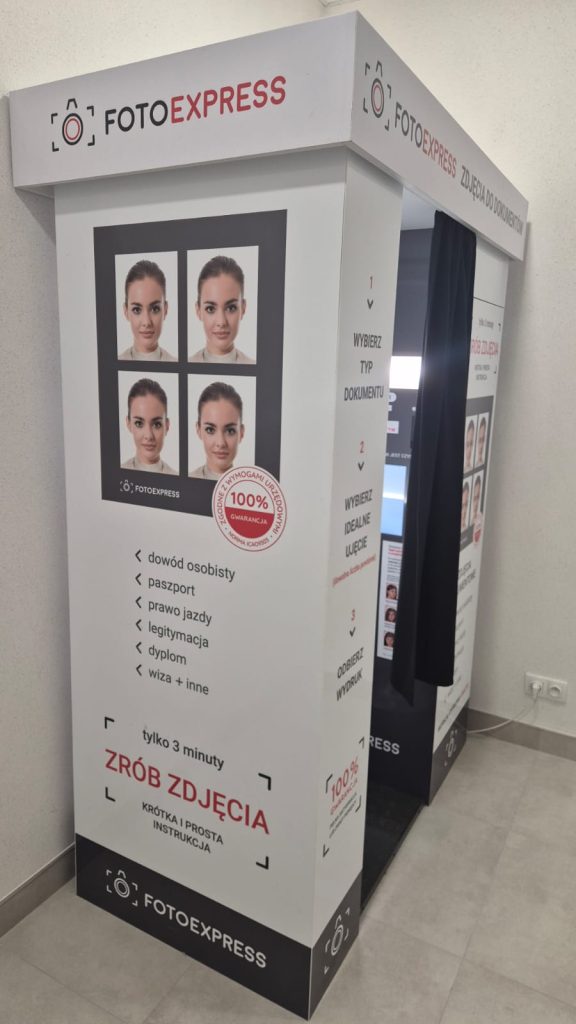 Budka fotograficzna FOTOEXPRESS z czarną zasłoną, białe ściany z czerwono-czarnym napisem i przykładowymi zdjęciami do dokumentów oraz instrukcją wykonania zdjęcia.